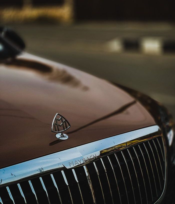 Close-up of a luxury car emblem on the hood of a Mercedes Maybach, highlighting elegance.