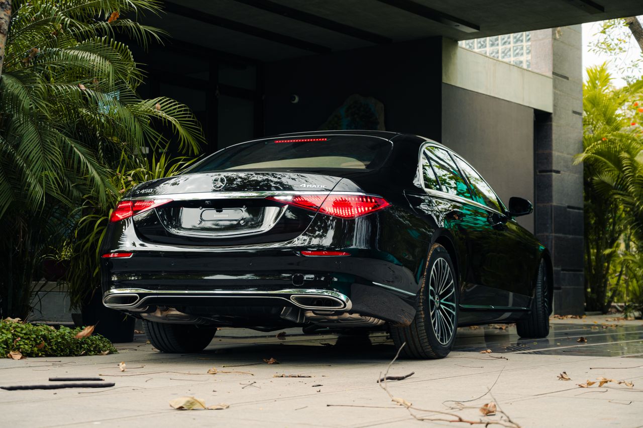 Elegant black luxury car parked outside a modern building amidst lush greenery.